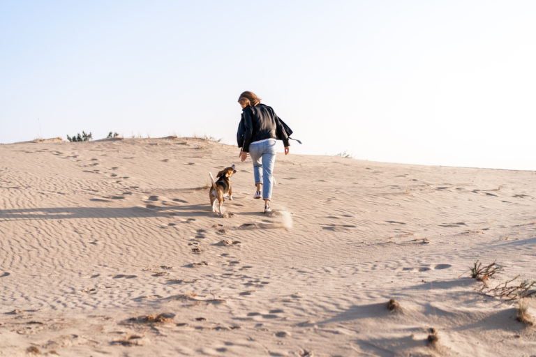 Chien qui court dans le sable à côté de sa maîtresse
