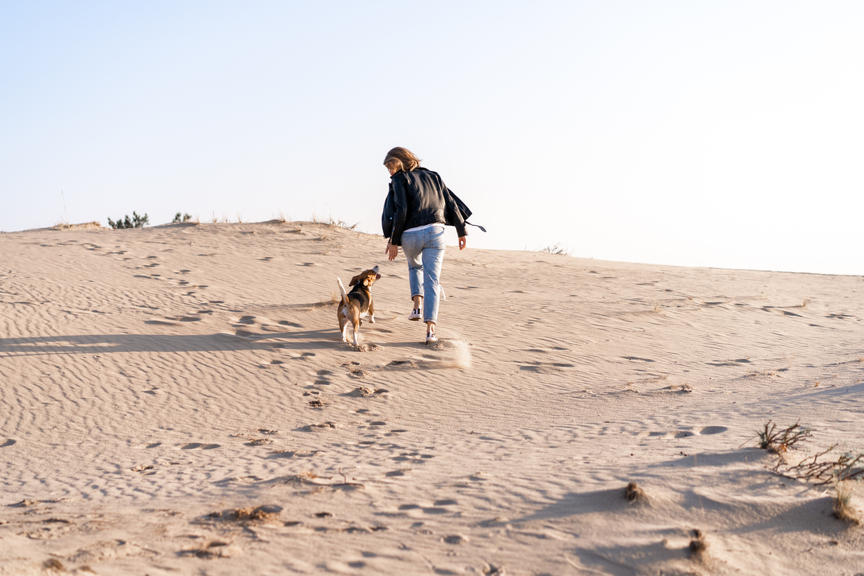 Chien qui court dans le sable à côté de sa maîtresse